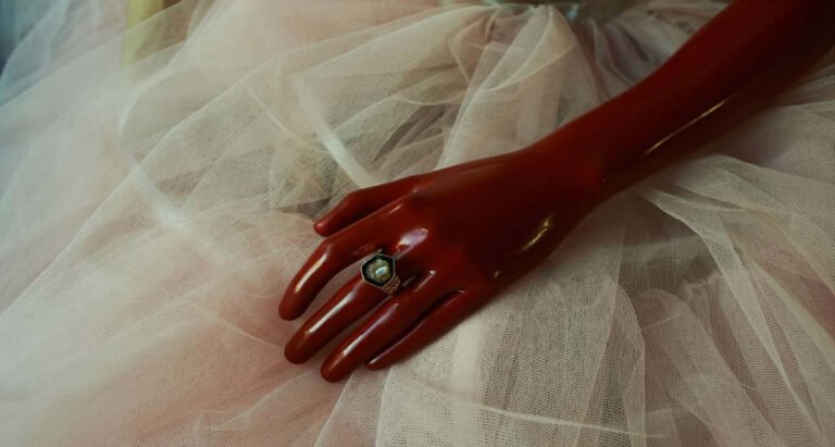 Red-gloved hand and ring resting across pale tulle