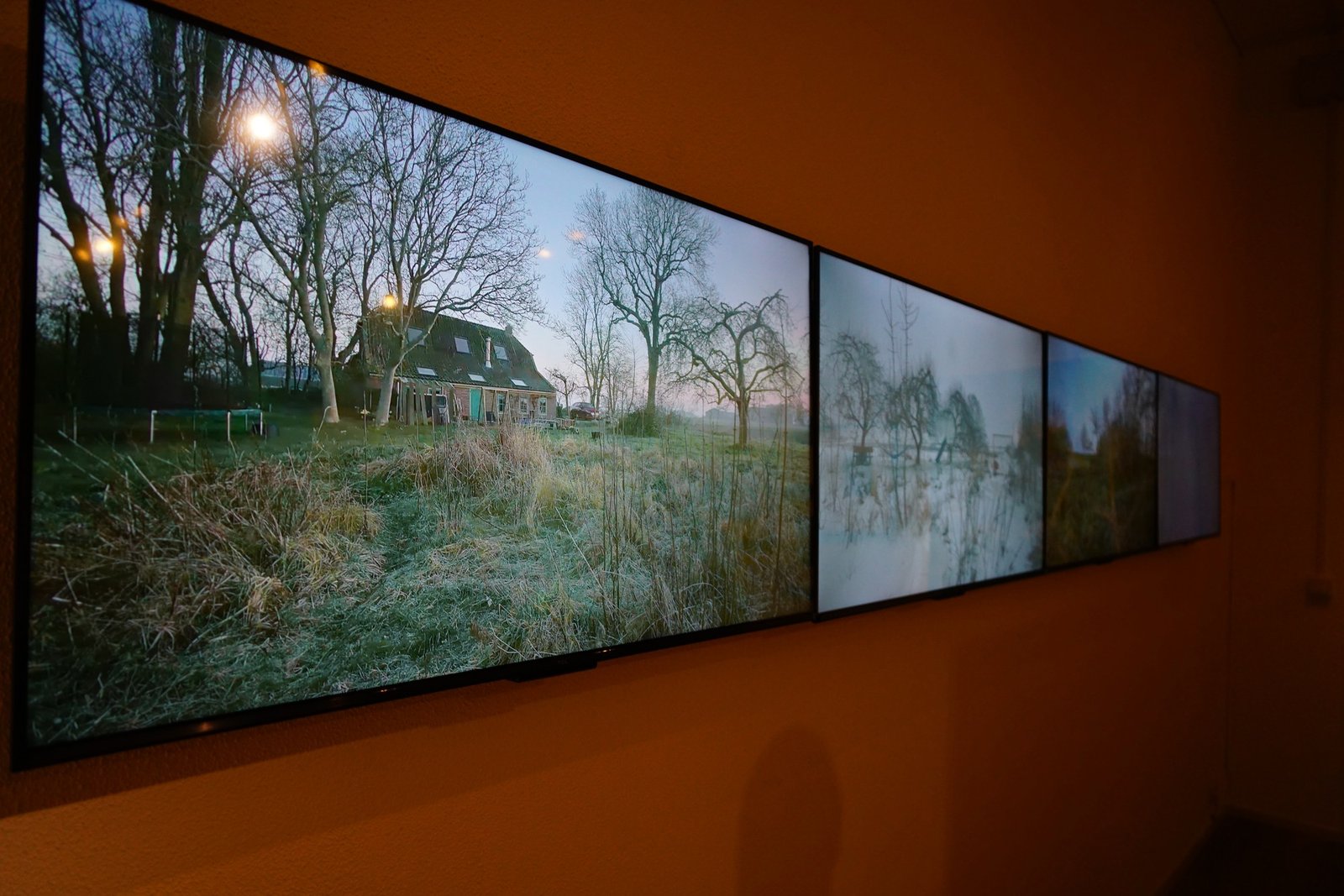 Four screens display garden views along an orange wall at the Steendruk Museum.